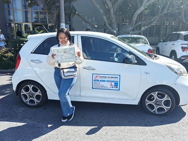 A+ learner holding a driving licence beside a training truck